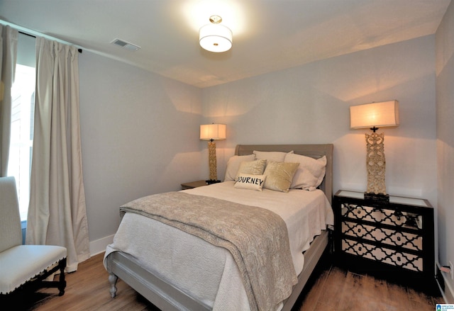 bedroom with baseboards, visible vents, and wood finished floors