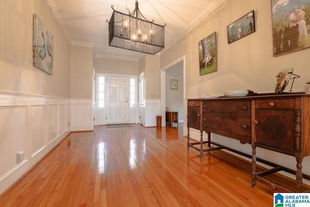 entryway with light wood-type flooring, ornamental molding, and a notable chandelier