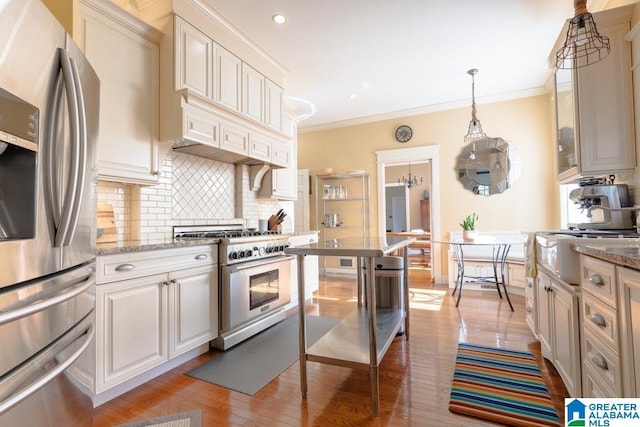 kitchen featuring light stone counters, crown molding, stainless steel appliances, hanging light fixtures, and decorative backsplash