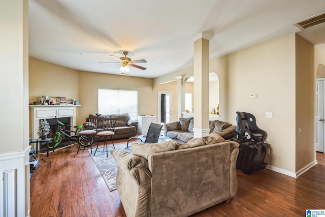 living room with dark wood-type flooring, ornate columns, and ceiling fan