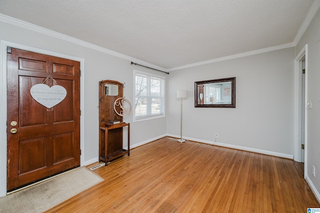 foyer entrance with light wood-type flooring, crown molding, a textured ceiling, and baseboards