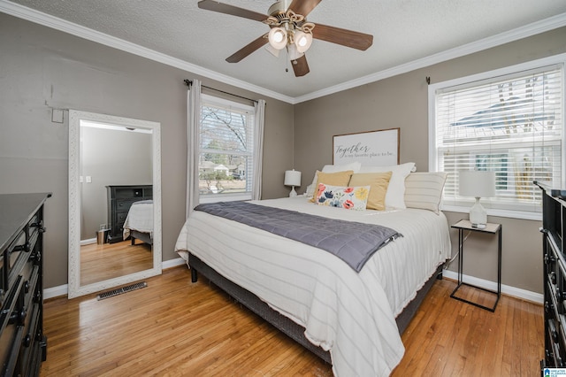 bedroom with visible vents, ornamental molding, a textured ceiling, light wood-type flooring, and baseboards