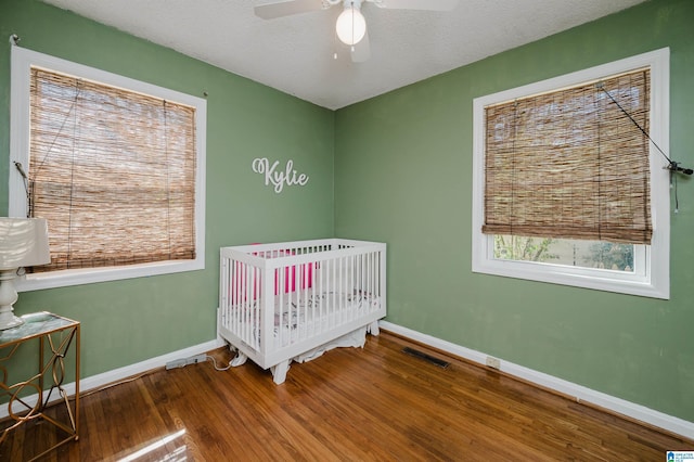 bedroom featuring baseboards, visible vents, wood finished floors, a textured ceiling, and a nursery area