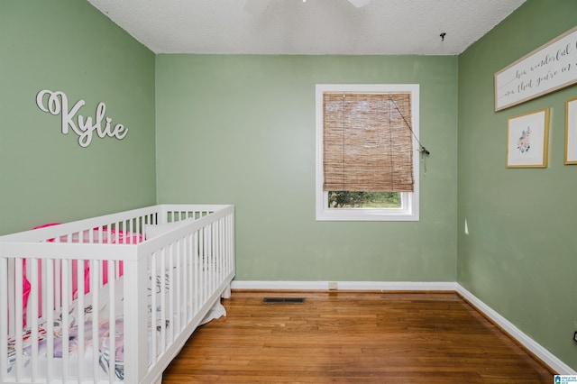 unfurnished bedroom with a nursery area, visible vents, baseboards, and wood finished floors