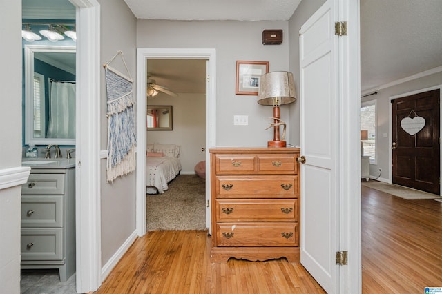 hall featuring a sink, light wood-style flooring, and baseboards