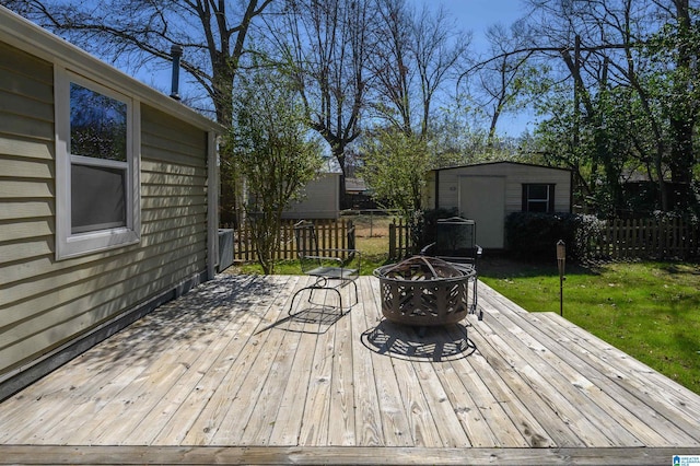 wooden terrace featuring a fire pit, a storage unit, an outdoor structure, and fence