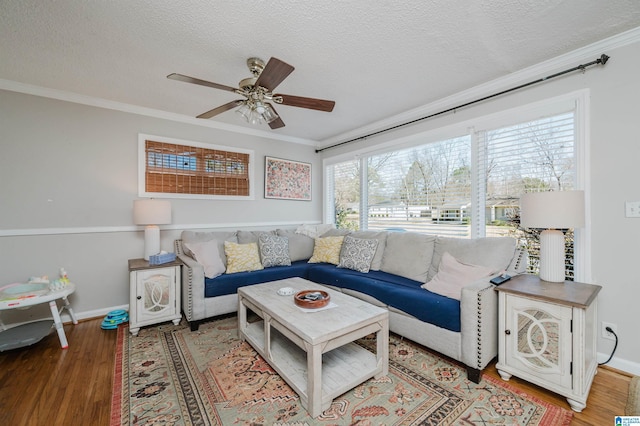 living room with a ceiling fan, a textured ceiling, ornamental molding, and wood finished floors