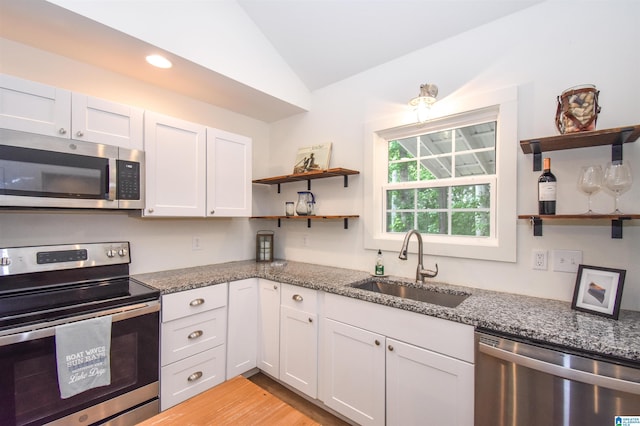 kitchen with appliances with stainless steel finishes, open shelves, a sink, vaulted ceiling, and dark stone counters