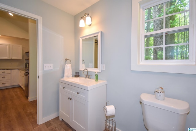 half bathroom featuring wood finished floors, toilet, vanity, and baseboards