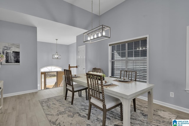 dining room featuring a towering ceiling, light wood-style flooring, and baseboards