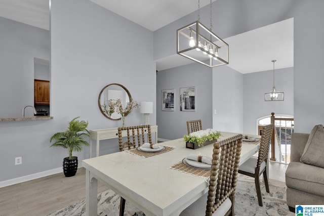 dining room with baseboards, a towering ceiling, light wood-style flooring, and a notable chandelier