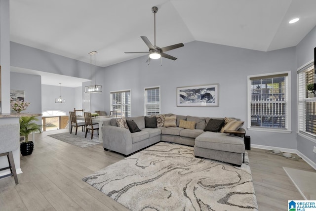 living area featuring high vaulted ceiling, light wood-style flooring, baseboards, and ceiling fan with notable chandelier