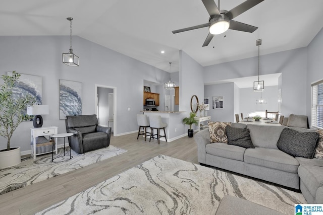 living area with high vaulted ceiling, baseboards, ceiling fan, and light wood finished floors