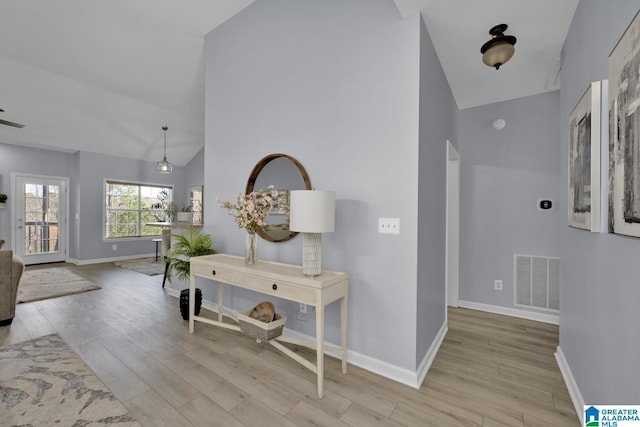 hall featuring light wood-style floors, lofted ceiling, visible vents, and baseboards