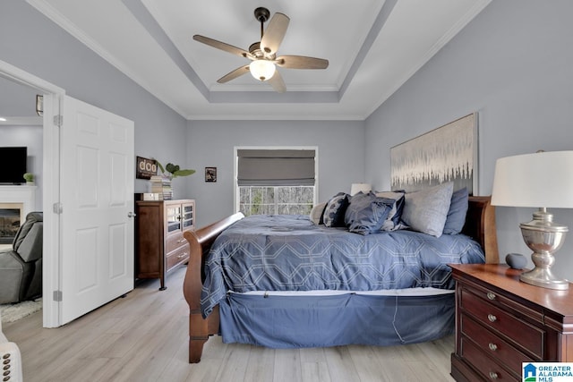 bedroom with light wood-type flooring, ceiling fan, ornamental molding, and a raised ceiling