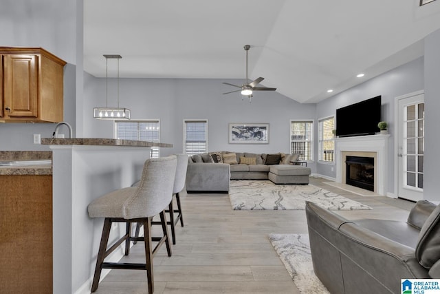 living room with baseboards, a ceiling fan, a glass covered fireplace, vaulted ceiling, and light wood-style floors