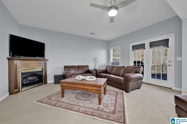 carpeted living room with ceiling fan, a glass covered fireplace, visible vents, and baseboards