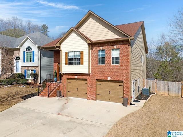 split foyer home featuring a garage, concrete driveway, fence, central AC, and brick siding