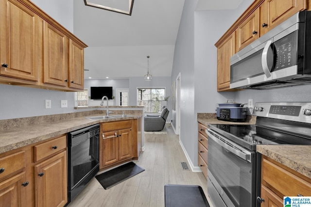 kitchen featuring light wood finished floors, light countertops, appliances with stainless steel finishes, brown cabinetry, and a sink