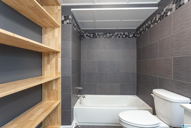 bathroom with tile walls, tiled shower / bath combo, and toilet