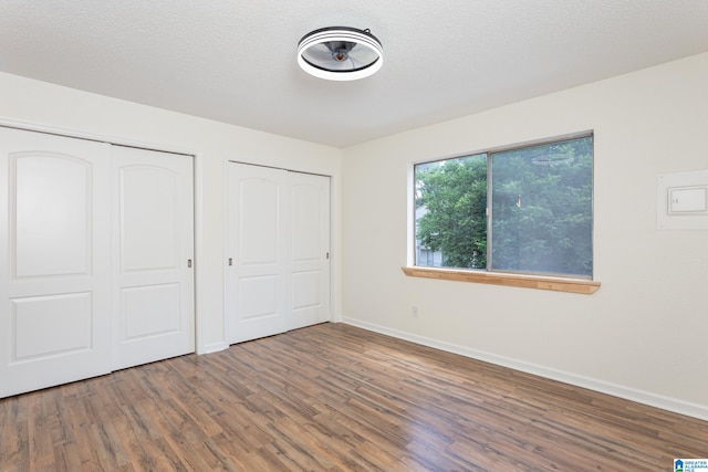 unfurnished bedroom with multiple closets, wood-type flooring, and a textured ceiling