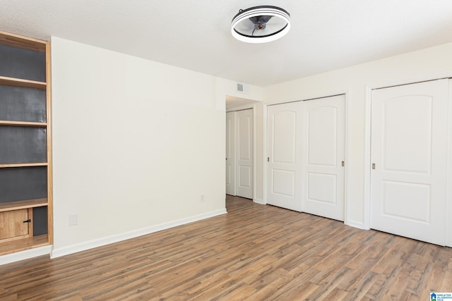 unfurnished bedroom featuring multiple closets and hardwood / wood-style floors