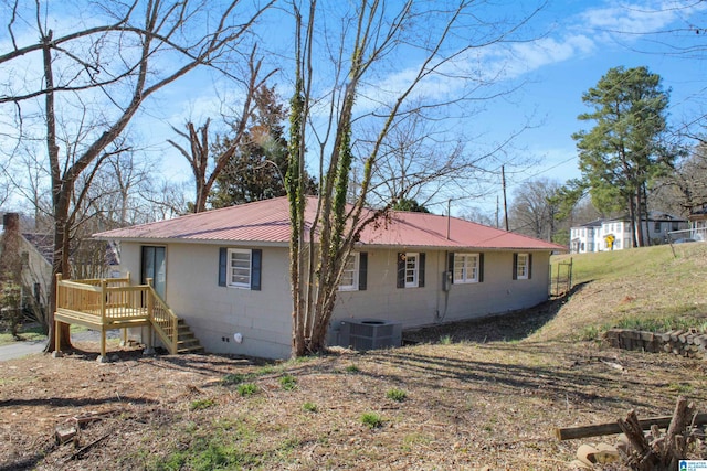 view of side of home with concrete block siding, metal roof, stairs, cooling unit, and a wooden deck