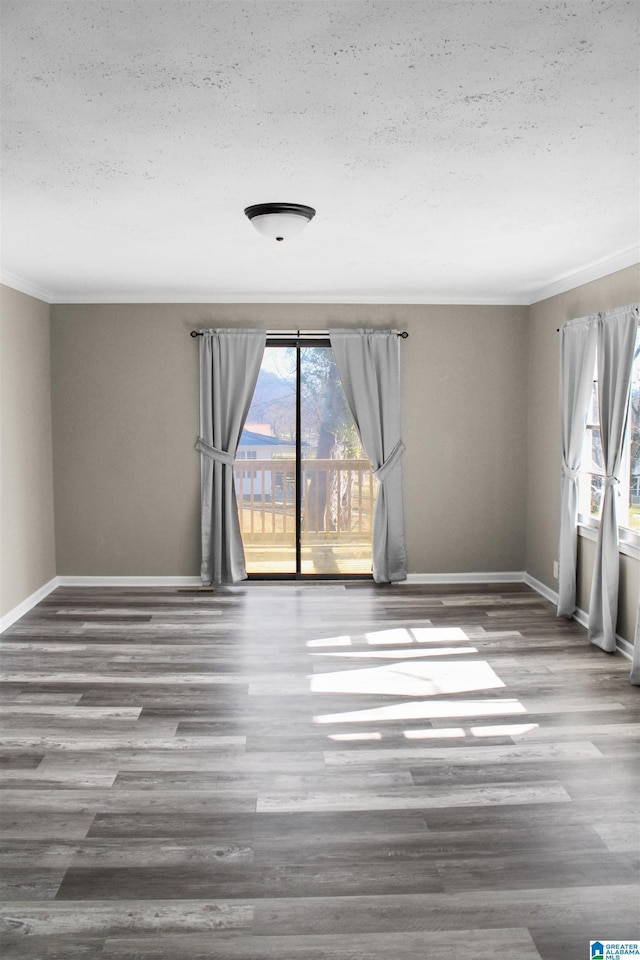 empty room with a textured ceiling, crown molding, wood finished floors, and baseboards