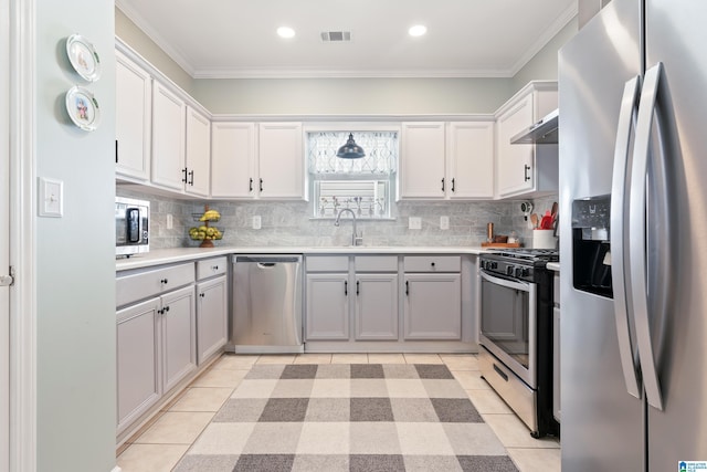 kitchen with appliances with stainless steel finishes, light countertops, under cabinet range hood, a sink, and light tile patterned flooring