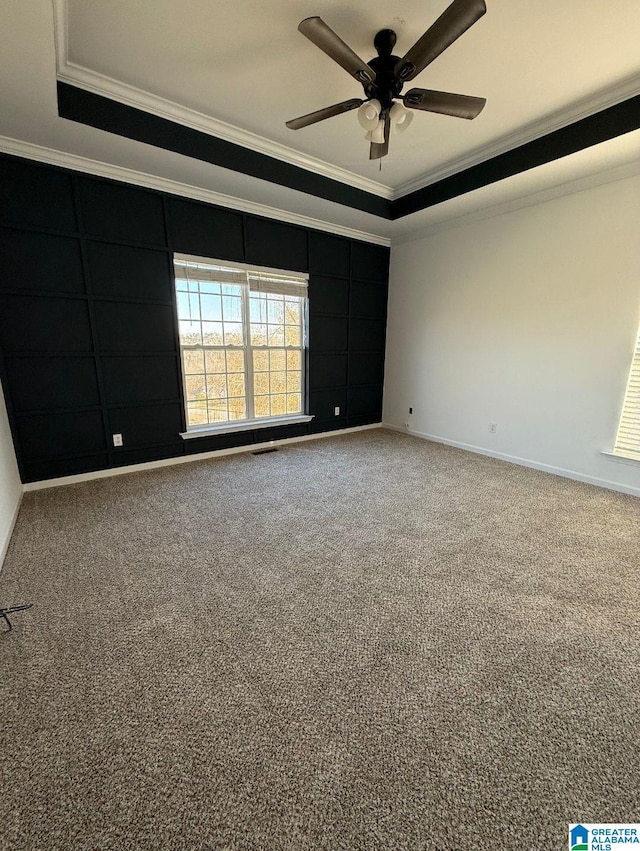 empty room with carpet, a raised ceiling, crown molding, and baseboards