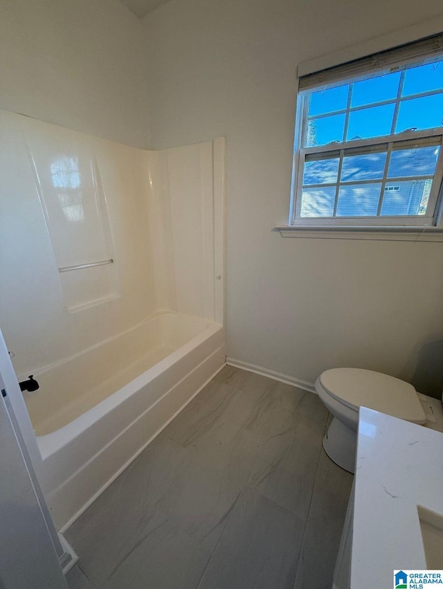 bathroom with baseboards, shower / bath combination, toilet, and a healthy amount of sunlight