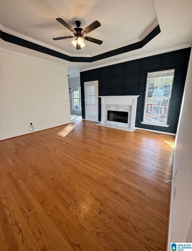 unfurnished living room featuring crown molding, a tray ceiling, wood finished floors, and a high end fireplace