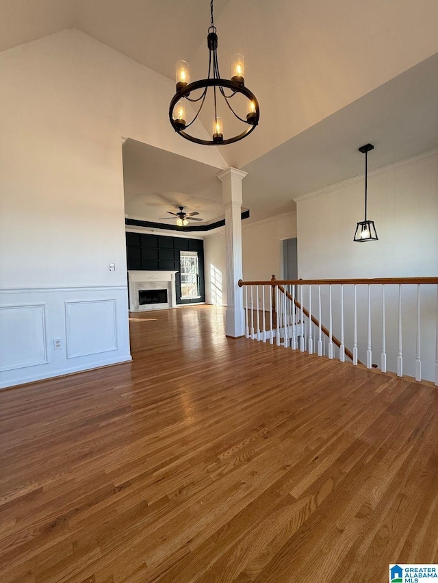 unfurnished room featuring ceiling fan with notable chandelier, a fireplace, wood finished floors, and decorative columns