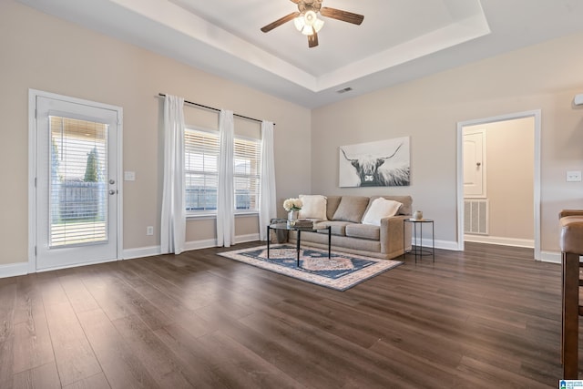 living room featuring a raised ceiling, ceiling fan, and dark hardwood / wood-style flooring