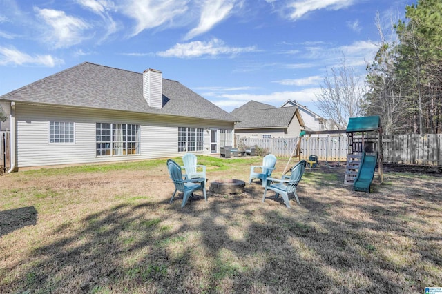 back of house featuring a playground, an outdoor fire pit, and a lawn