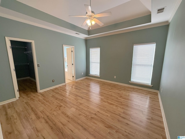 unfurnished bedroom with crown molding, a spacious closet, a tray ceiling, and light wood-style floors