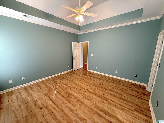 unfurnished bedroom featuring light wood-style floors, a tray ceiling, crown molding, and baseboards