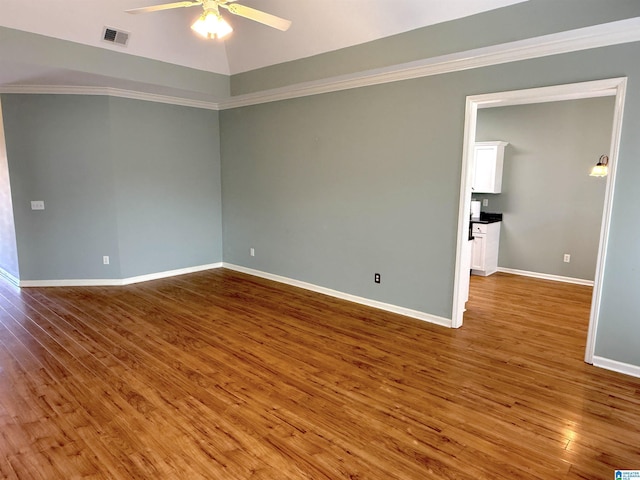 empty room featuring visible vents, crown molding, baseboards, and wood finished floors