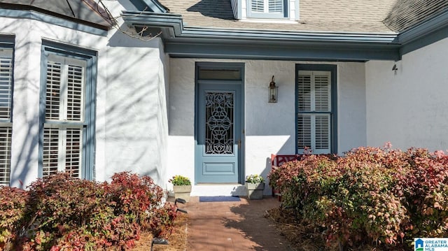 view of exterior entry with stucco siding and roof with shingles