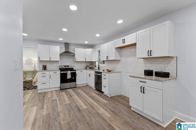 kitchen with appliances with stainless steel finishes, sink, light hardwood / wood-style flooring, wall chimney exhaust hood, and white cabinets