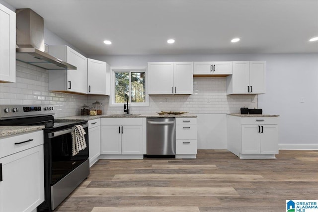 kitchen featuring light wood-type flooring, stainless steel appliances, sink, white cabinets, and wall chimney exhaust hood