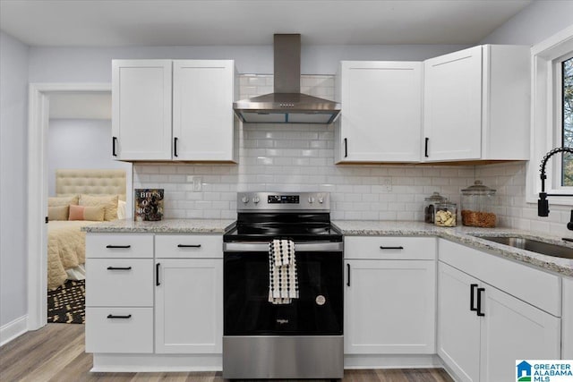 kitchen with stainless steel electric range oven, white cabinetry, wall chimney exhaust hood, and sink