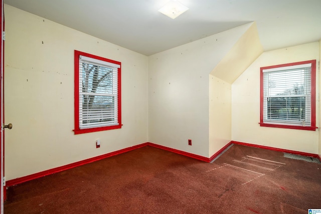 additional living space with plenty of natural light, dark colored carpet, and vaulted ceiling