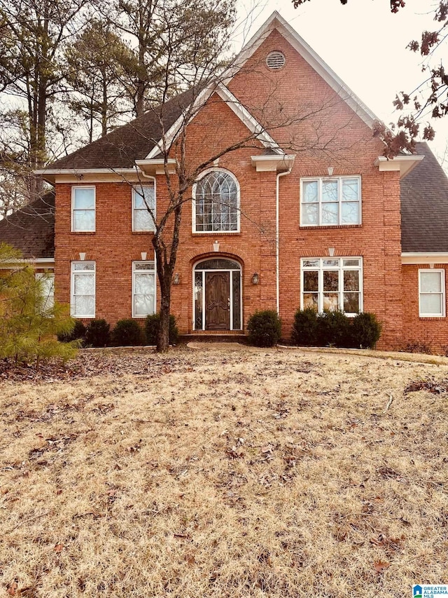 colonial home with brick siding and a shingled roof