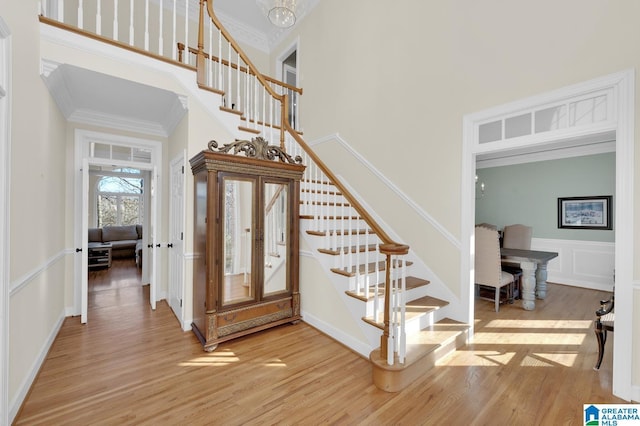 entrance foyer featuring crown molding, a decorative wall, a towering ceiling, light wood-style floors, and stairs