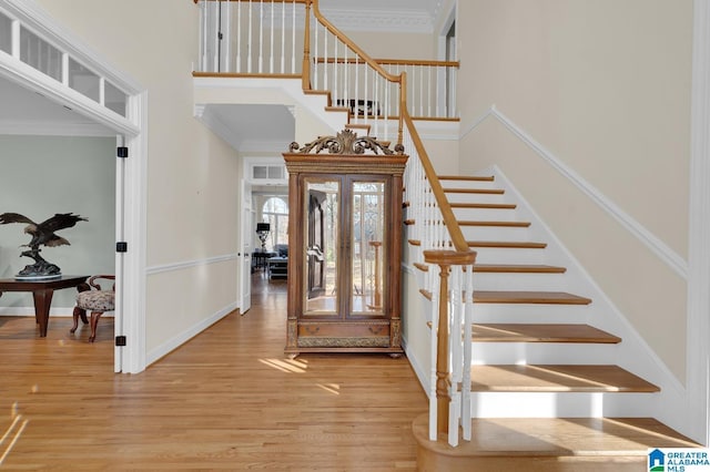 entrance foyer with crown molding, a high ceiling, light wood-style floors, baseboards, and stairs