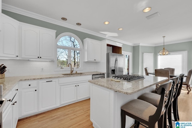 kitchen featuring appliances with stainless steel finishes, a breakfast bar, ornamental molding, light wood-style floors, and a sink