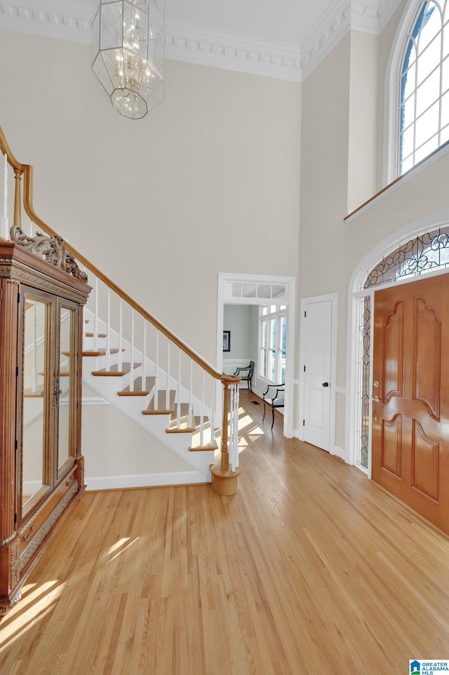 foyer entrance featuring crown molding, an inviting chandelier, wood finished floors, plenty of natural light, and stairs