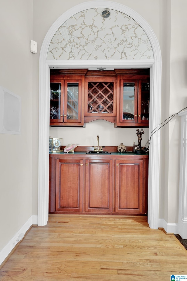 bar with light wood finished floors, indoor wet bar, a sink, and baseboards