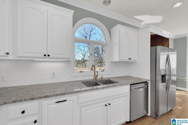 kitchen with light stone counters, appliances with stainless steel finishes, ornamental molding, white cabinetry, and a sink